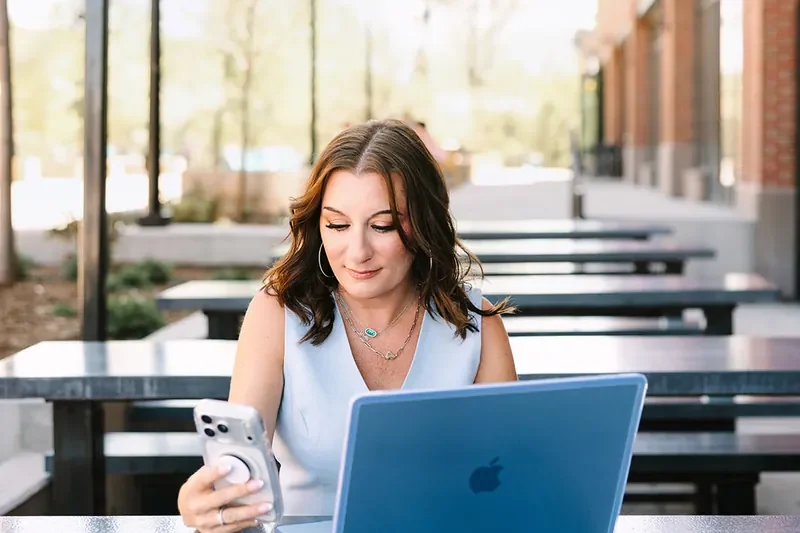 Jessica Lentz working at her laptop with her phone in hand at an outdoor table in Castle Rock