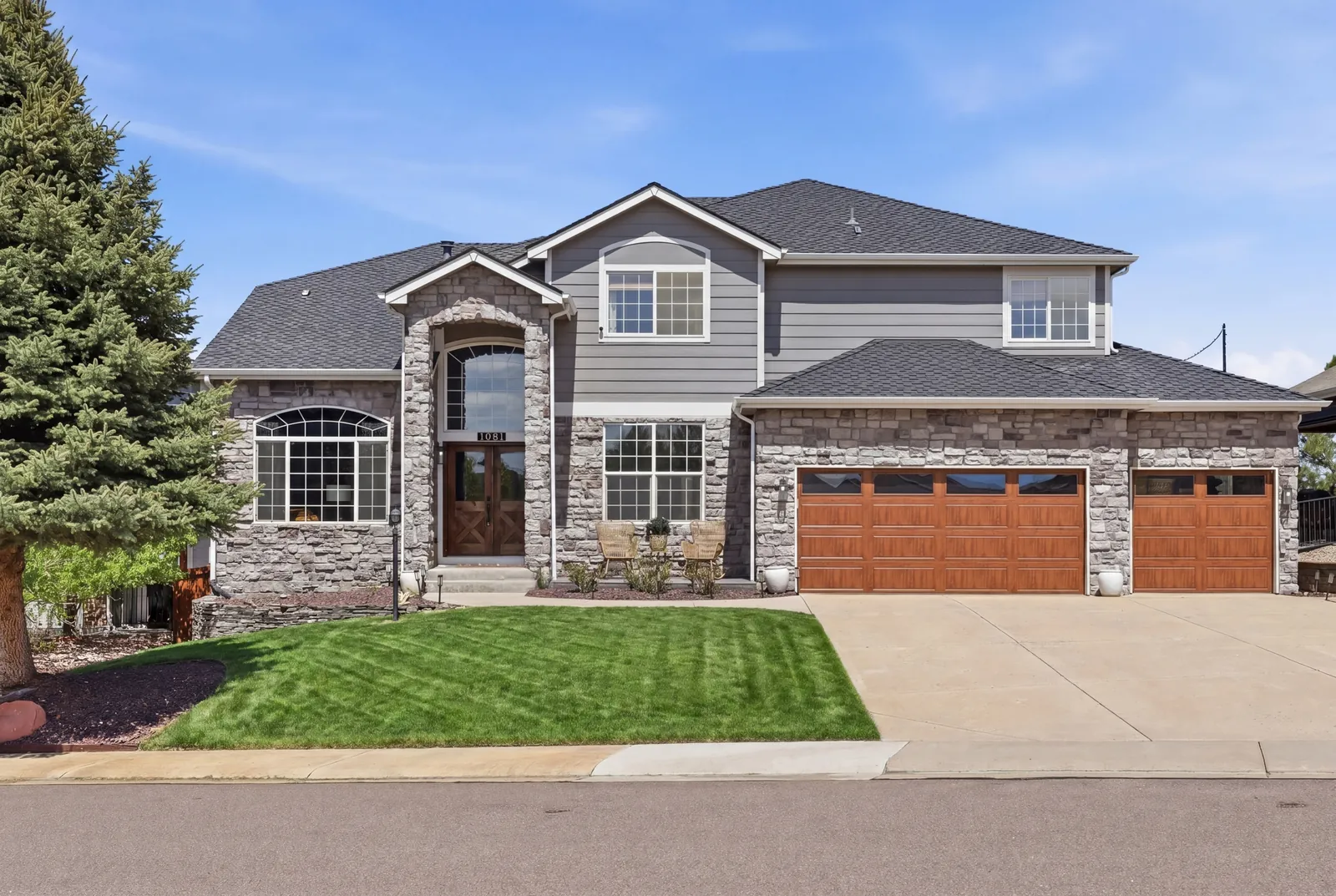 Castle Rock stone-and-siding home with three-car wood-paneled garage and manicured spring lawn