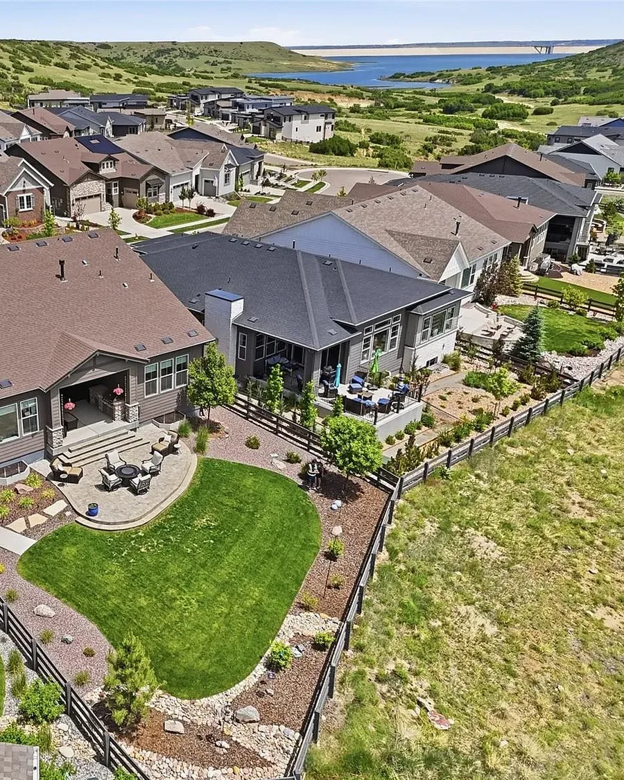 Aerial view of a landscaped backyard and neighborhood with a reservoir beyond in Castle Pines, one of Jessica's listings