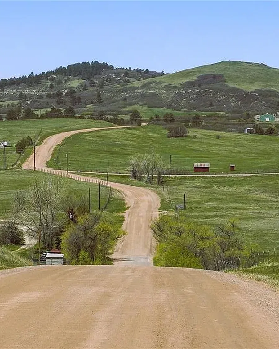A gravel road winding through green pastures and rolling hills near Larkspur, Colorado